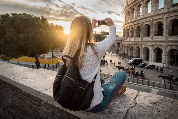 Woman tourist selfie with phone camera in hands near the Coliseu Woman tourist selfie with phone camera in hands near the Coliseum in Rome under sunlight and blue sky. Famous popular touristic place in the world.